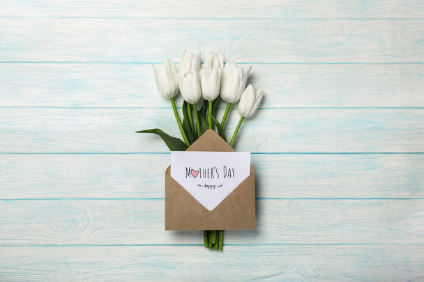 A bouquet of white tulips with a love note and envelope on blue wooden boards. Top view with place for your congratulations. Mother's day. - Fotografie, Obrázek