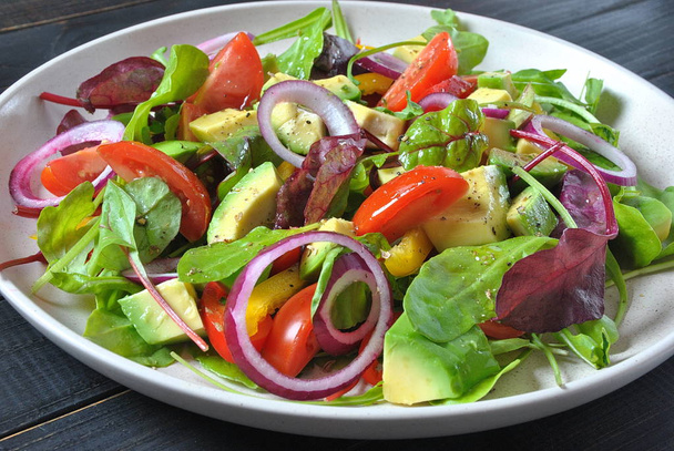 Fresh avocado salad with cherry tomatoes, red onion, arugula beet leaves, yellow sweet pepper on the black wooden background. Healthy food concept. Vegan food. - Φωτογραφία, εικόνα