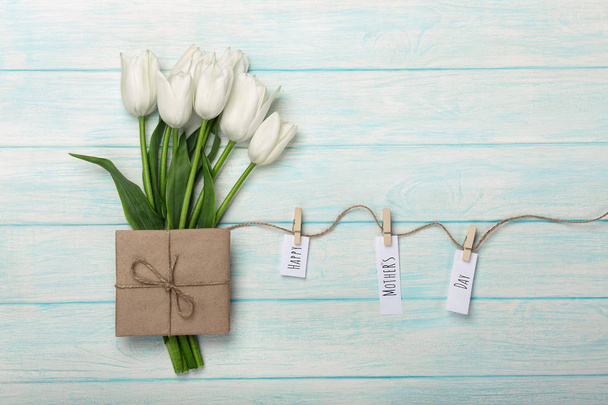A bouquet of white tulips and envelope with a stickers with clothespins on a rope and blue wooden boards. Top view with place for your congratulations. Mother's day. - Фото, изображение