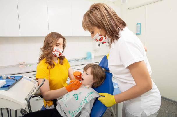 Стоматолог вивчає зуби хлопчиків у клініці. Маленький пацієнт у стоматологічному кріслі посміхається
. - Фото, зображення