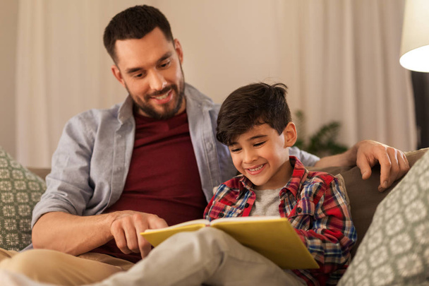 happy father and son reading book sofa at home - Foto, Imagem