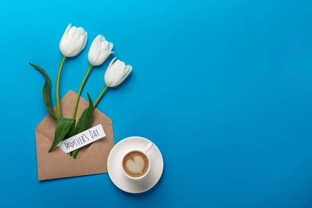 White tulips with cup of coffee, a love note and envelope on a blue background. Top view with place for your congratulations. Mother's day. - 写真・画像