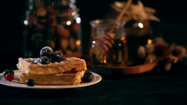 selective focus of sugar powder sifting on Belgian waffles with berries on black background  - Кадры, видео