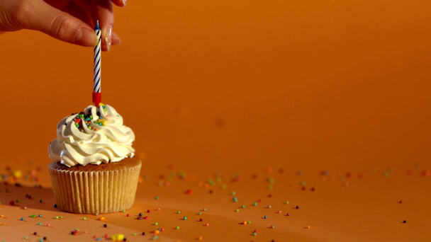 câmera lenta da mão feminina colocando vela no cupcake com creme branco no fundo laranja
 - Filmagem, Vídeo