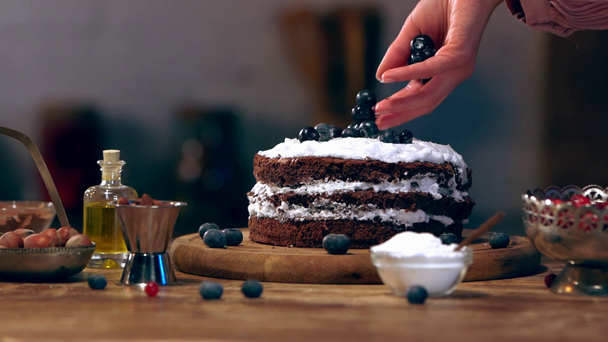 Slow-motion van vrouwelijke kok verstrooiing bessen op taart op houten tafel met ingrediënten - Video