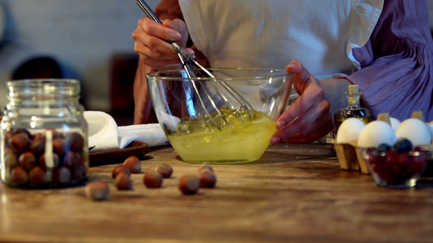 slow motion of female cook whipping eggs with balloon whisk in glass bowl - Materiaali, video