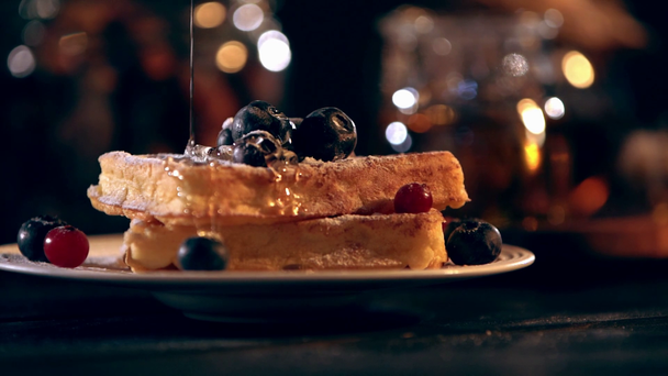 selective focus of viscous honey dripping on Belgian waffles with blueberries and bokeh lights on background - Footage, Video