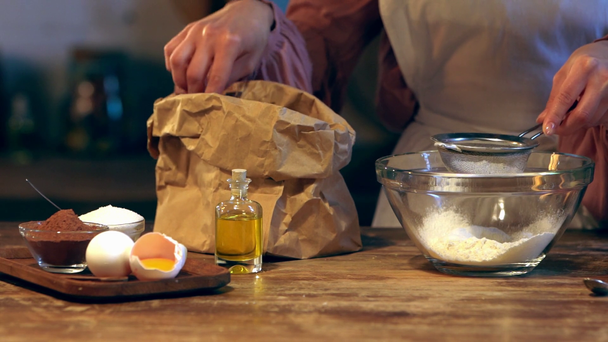 Slow-motion van vrouwelijke kok zeven meel in glazen kom aan houten tafel - Video