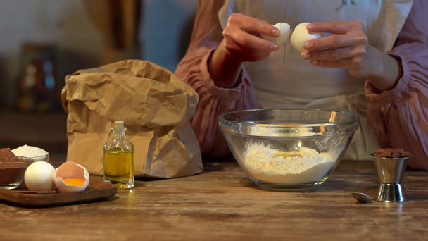 αργή κίνηση της γυναικείας μάγειρας σπάζοντας το αυγό σε γυάλινο μπολ με το αλεύρι στο ξύλινο τραπέζι  - Πλάνα, βίντεο