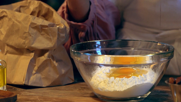 zwolnionym tempie kobiece Cook, rozbijając i dodając jajko w szklanej misce z mąki  - Materiał filmowy, wideo