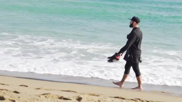 Ένας άντρας με ρούχα περπατώντας στην ακτή των ένα κρύο και κυματιστή θάλασσα για: Βαρκελώνη - Πλάνα, βίντεο