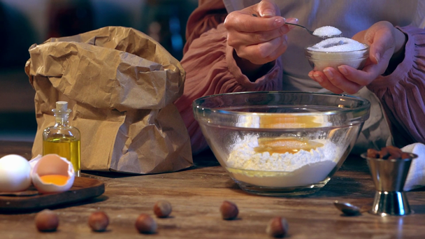 hidasliikkeinen naispuolinen kokki lisäämällä sokeria kulhoon jauhoja ja munia
 - Materiaali, video