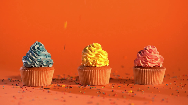ralenti des arrosages sucrés tombant sur des cupcakes multicolores sur fond orange
  - Séquence, vidéo