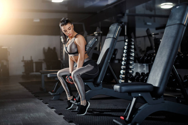 Karcsú, testépítő lány, nehéz súlyzót emel a tükör előtt, miközben edz az edzőteremben. Sport koncepció, zsírégetés és az egészséges életmód. - Fotó, kép
