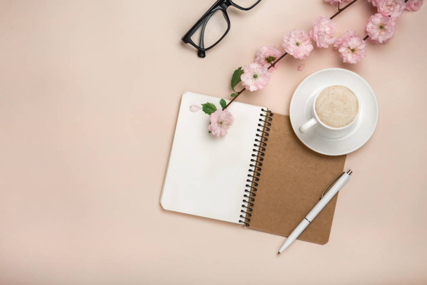 White cup with cappuccino, sakura flowers, notebook on a pastel pink background. Top view with space for your text. - Foto, Imagem