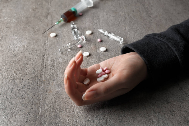 Жіноча рука з таблетками та шприцом на сірому фоні. концепція самогубства
 - Фото, зображення
