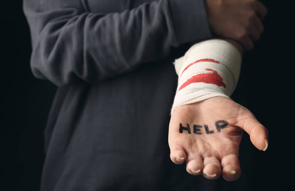 Woman with bloodstained bandage and word help written on her palm. Suicide awareness concept - Photo, image