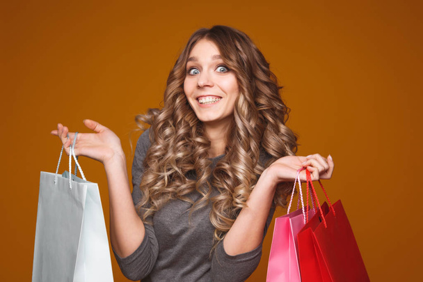 Picture of a cheerful young brunette woman in white summer dress holding credit card posing with shopping bags and looking at camera over pink background - Foto, Bild