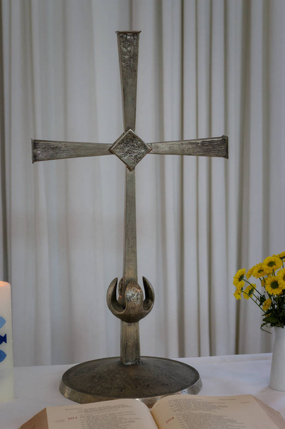 Pequeño altar con cruz santa, biblia abierta, vela de bautismo y flores en un jarrón
 - Foto, imagen