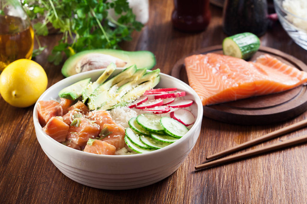 Poke bowl, traditional Hawaiian raw fish salad with rice, avocado, cucumber and radish on wooden background - Φωτογραφία, εικόνα