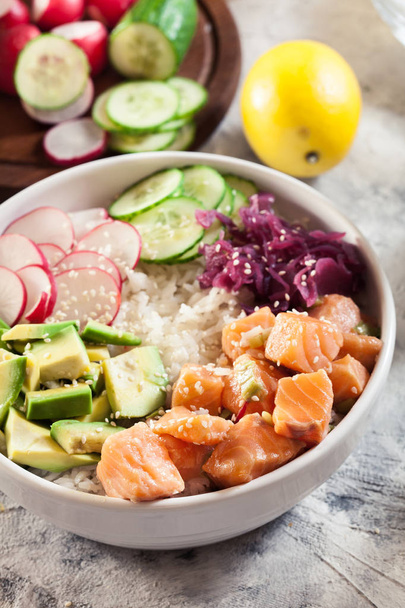 Poke bowl, traditional Hawaiian raw fish salad with rice, avocado, cucumber and radish on bright background - Fotó, kép