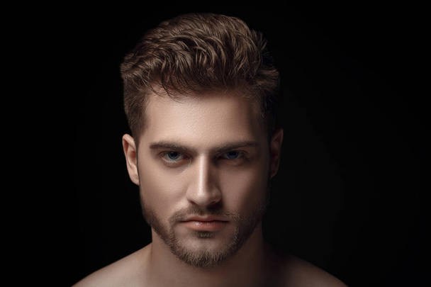 Closeup view portrait of one handsome bearded young macho man with strong look hazel eyes and sexy lips standing in light looking forward in studio on black background - Foto, immagini