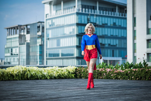 Full-length portrait of young attractive Caucasian woman in sexy superwoman costume walking down the street and looking at camera - Photo, Image