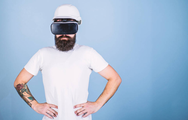 Man with beard in VR glasses serious and confident, light blue background. 3D design concept. Architect or engineer with virtual reality glasses. Guy in helmet works as engineer in virtual reality - Фото, зображення