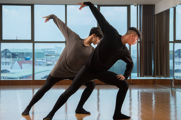 Dos chicos asiáticos bailando hermosa danza contemporánea al mismo tiempo cerca de enorme ventana en el estudio
 - Foto, imagen
