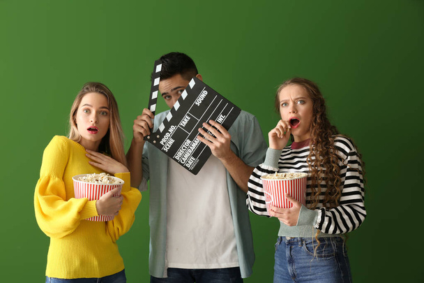 Scared young people with popcorn and movie clapper on color background - Photo, Image
