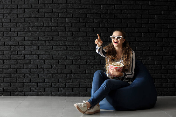 Fiatal nő, pattogatott kukorica, film, sötét tégla fal közelében - Fotó, kép