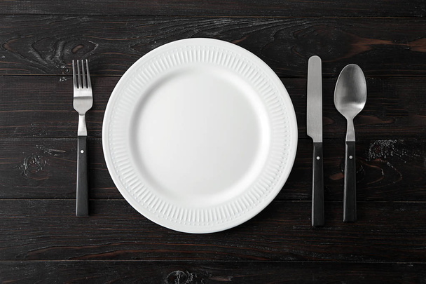 Empty ceramic plate with cutlery on dark wooden background - Фото, зображення