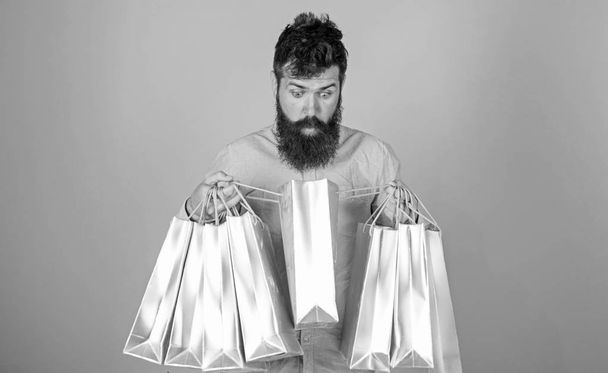 Sale and discount concept. Hipster on shocked face shopping addicted or shopaholic. Man with beard and mustache carry shopping bags, light blue background. Guy shopping on sales season with discounts - Valokuva, kuva