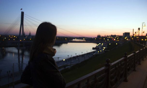 Young woman watching the sunset over the river in the city on the bridge in the background. - 写真・画像