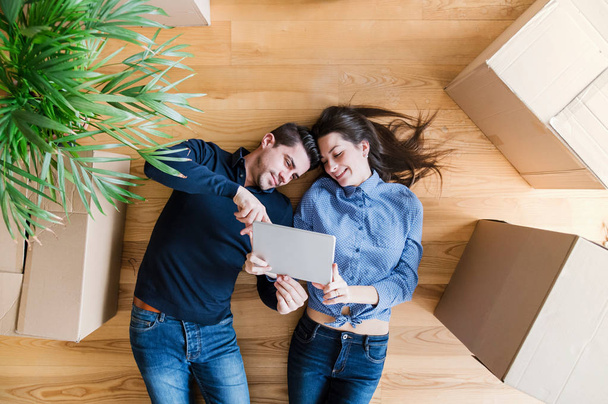 A top view of young couple with tablet and cardboard boxes moving in a new home. - Fotoğraf, Görsel