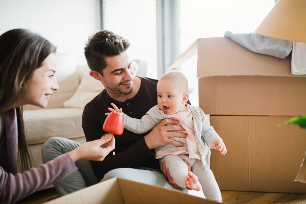 Young couple with a baby and cardboard boxes moving in a new home. - Foto, Bild