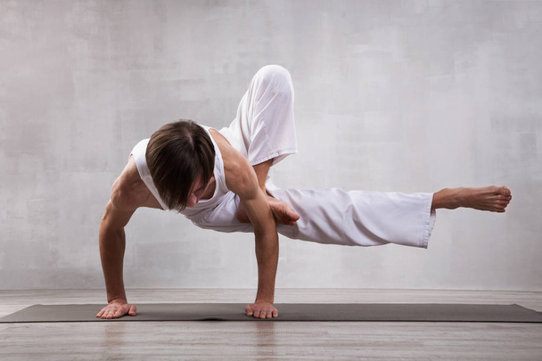 Young man in white clothes practicing yoga. Dragonfly pose - Zdjęcie, obraz