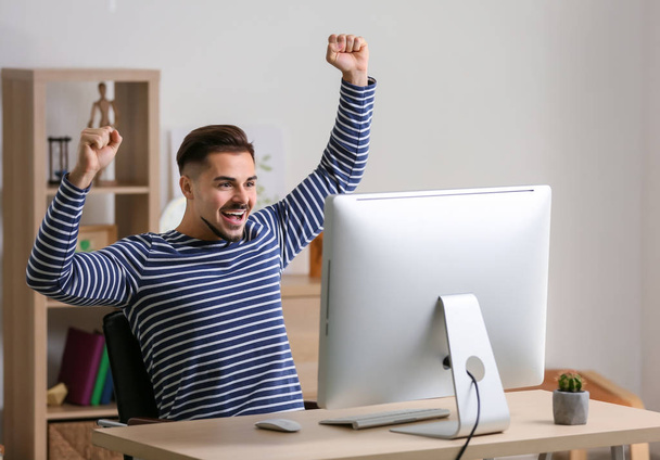 Onnellinen nuori mies voitettuaan tietokonepelin kotona
 - Valokuva, kuva