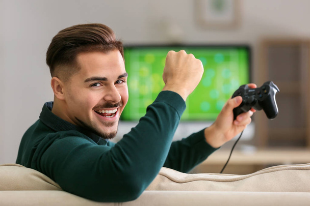 Onnellinen nuori mies voitettuaan videopelin kotona
 - Valokuva, kuva
