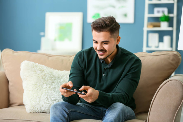 Young man playing game on smartphone at home - Foto, Imagen