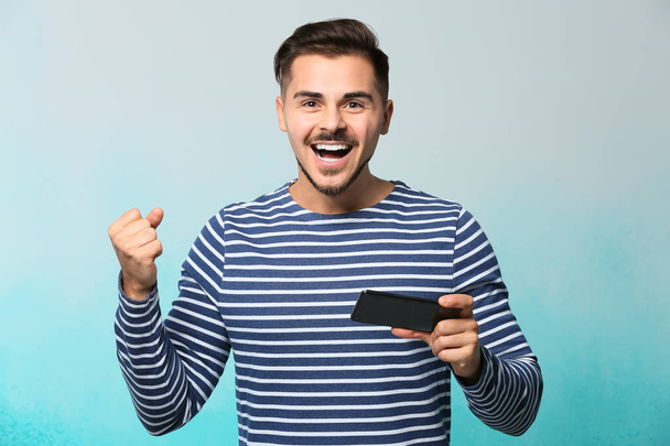 Onnellinen nuori mies voitettuaan pelin älypuhelimella väritaustaa vasten
 - Valokuva, kuva