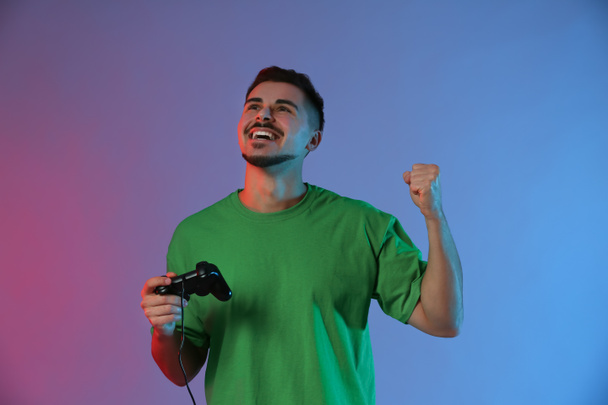 Gelukkig jonge man na winnende video wedstrijd op kleur achtergrond - Foto, afbeelding