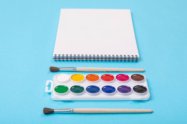 Набор акварельных красок с кисточками и альбом для рисования на синем фоне
 - Фото, изображение