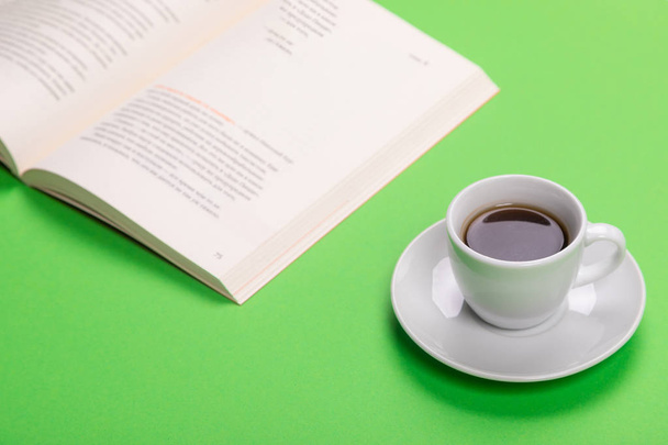 Working table with cup of coffee and book isolated on green background - 写真・画像