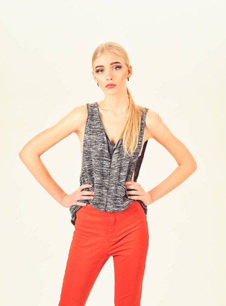 Skinny model with thick eyebrows and neat ponytail wearing melange gray sleeveless blouse and bright orange pants isolated on white background - Fotó, kép