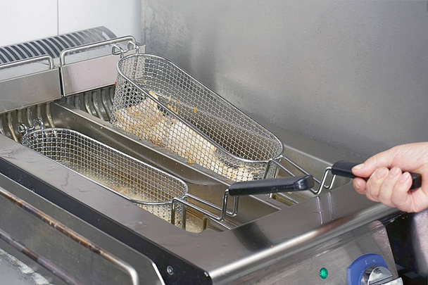 El cocinero fríe el pescado en una freidora. Preparación en freidora. Freidora con aceite hirviendo en la cocina del hotel restaurante
 - Foto, Imagen