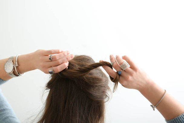 Όμορφη νεαρή γυναίκα με το κομψό κοσμήματος που κάνει τα μαλλιά της σε άσπρο φόντο - Φωτογραφία, εικόνα