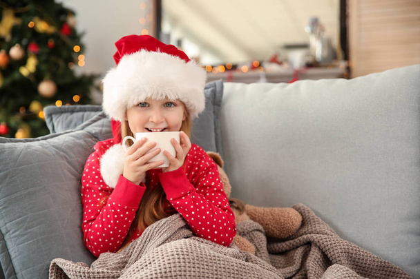 Aranyos kislány iszik forró csokoládé otthon, karácsony előestéjén Santa kalap - Fotó, kép