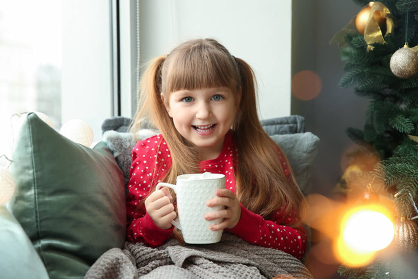 Cute little girl drinking hot chocolate at home on Christmas eve - Фото, зображення