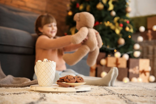 Xícara de chocolate quente e prato com biscoitos no chão no quarto da menina
 - Foto, Imagem